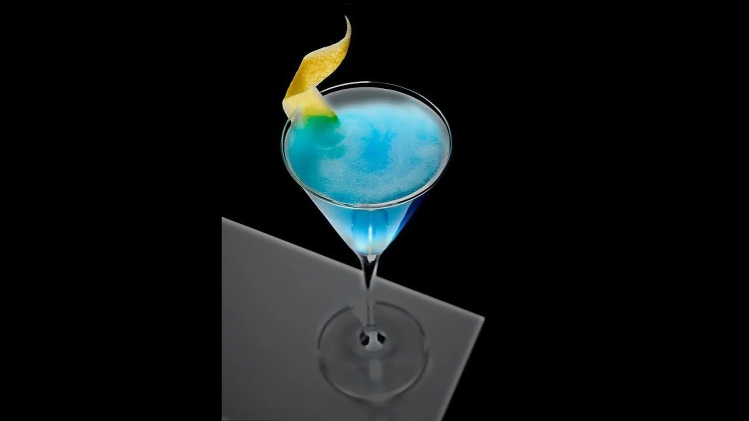 Cocktail Angelo Azzurro blu elettrico servito in coppetta Martini con zest di limone, su fondo scuro