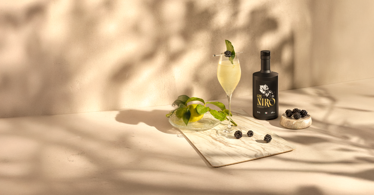 Cocktail Niro 75 giallo brillante con menta in coppetta accanto alla bottiglia GIN NIRO e olive nere