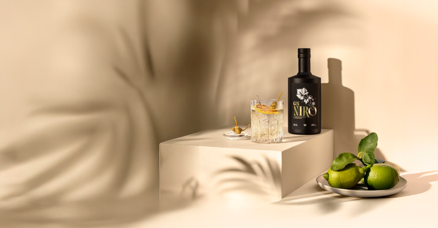 Cocktail Nironi bianco con olive verdi e lime accanto alla bottiglia GIN NIRO