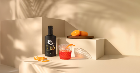 Cocktail Nironi rosso con scorza d'arancia accanto alla bottiglia GIN NIRO e arance fresche